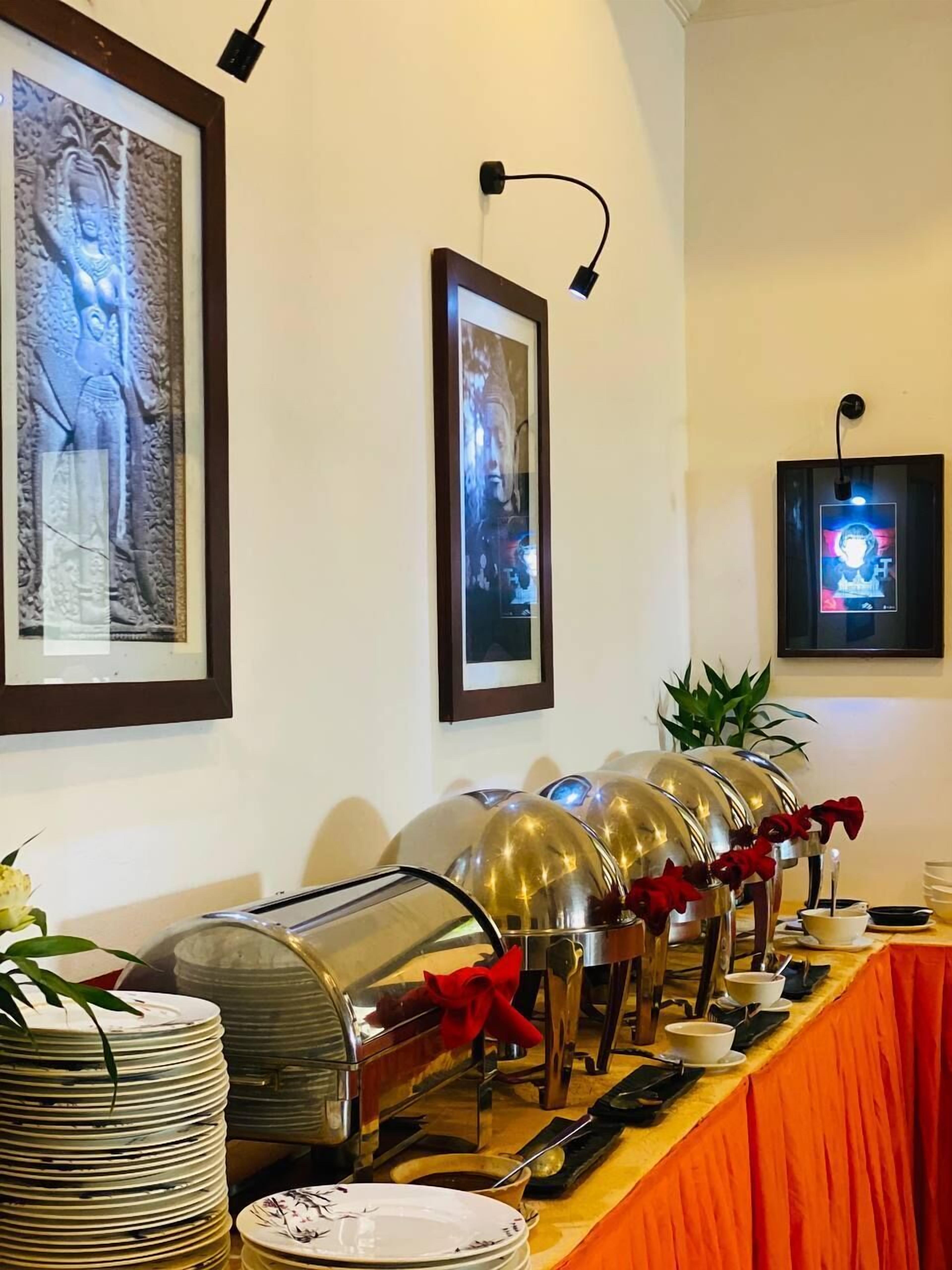 A buffet setup with multiple food stations, framed artwork on the wall, and a table with a red tablecloth.