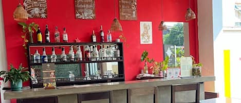Zona de bar con pared roja, varios taburetes y una barra con diferentes botellas.