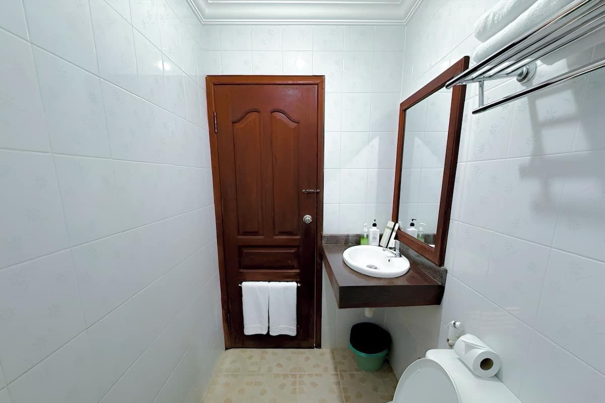 Ein kleines Badezimmer mit Holztür, weißen Fliesenwänden, einem weißen Waschbecken, einem Spiegel und einer Toilette.