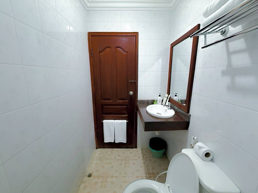 A small bathroom with a wooden door, white tiled walls, a white sink, a mirror, and a toilet.