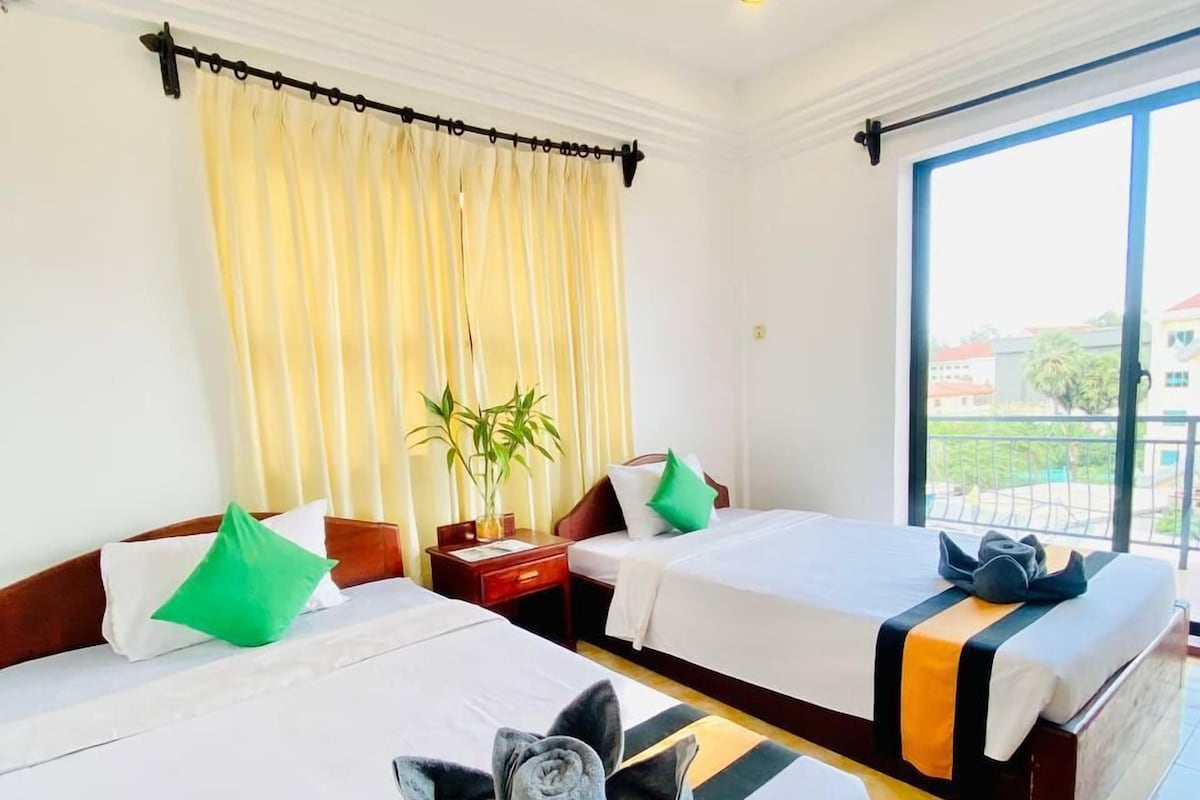 A hotel room with two beds, a large window, a potted plant, and a view of the outside.