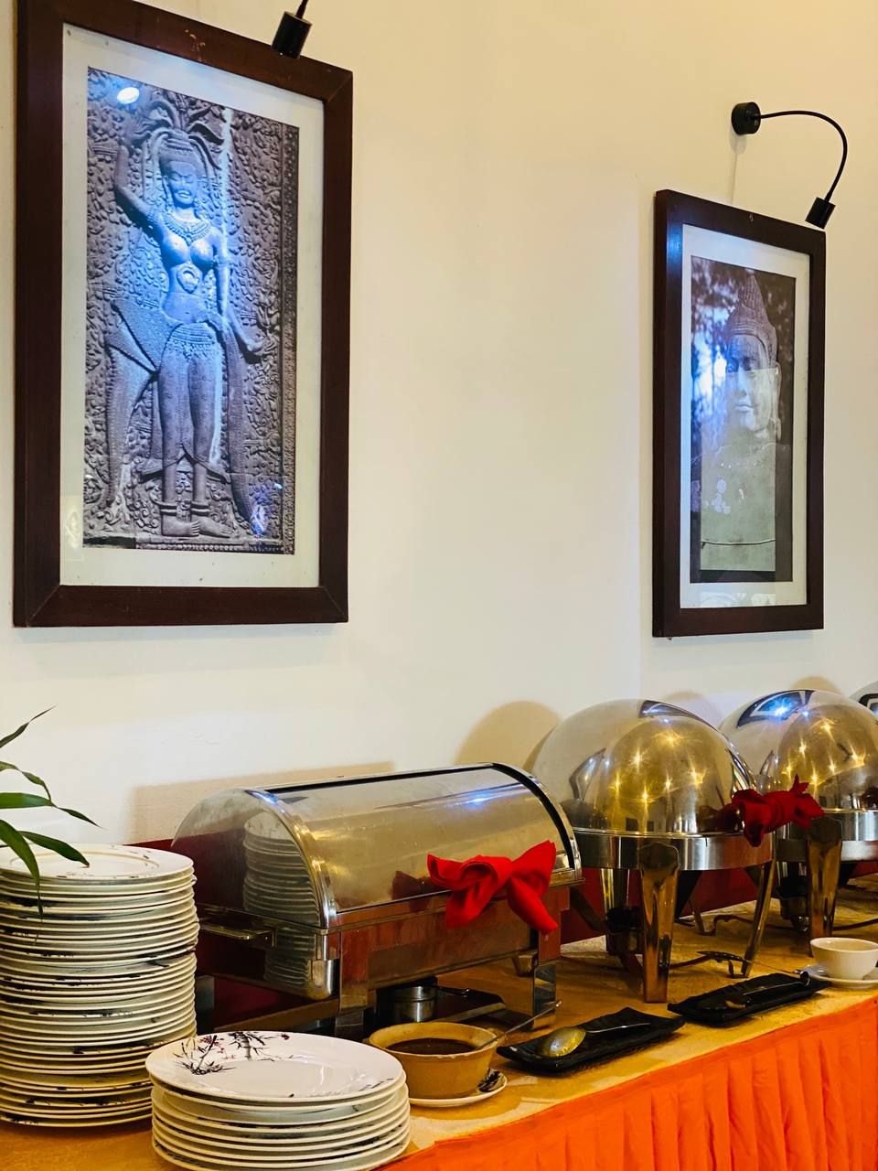 A buffet setup with stacked plates, a food station, and two framed pictures on the wall.