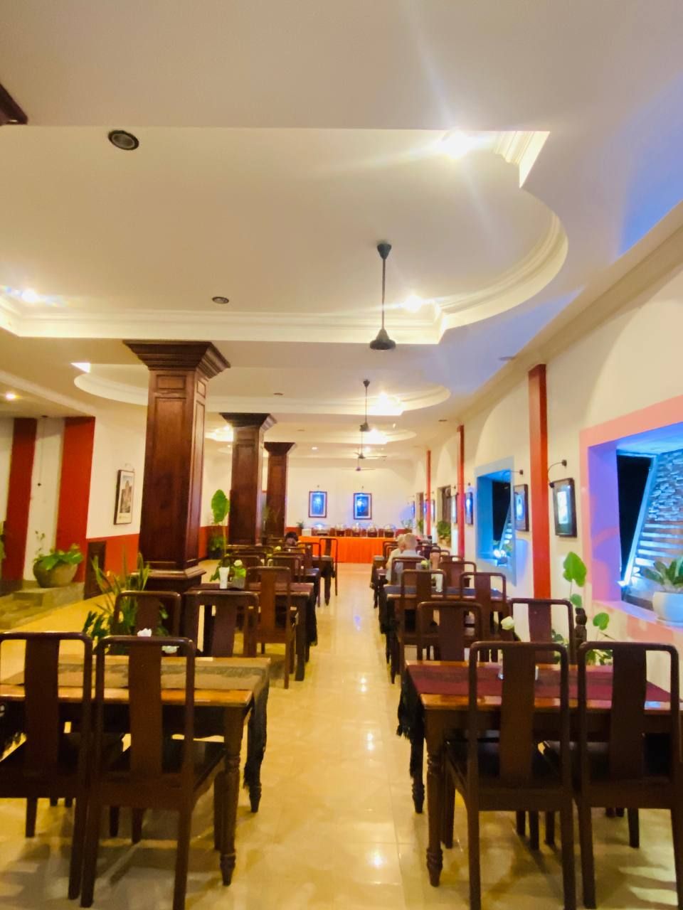 A spacious dining area with wooden tables and chairs, a central counter, and ceiling fans.