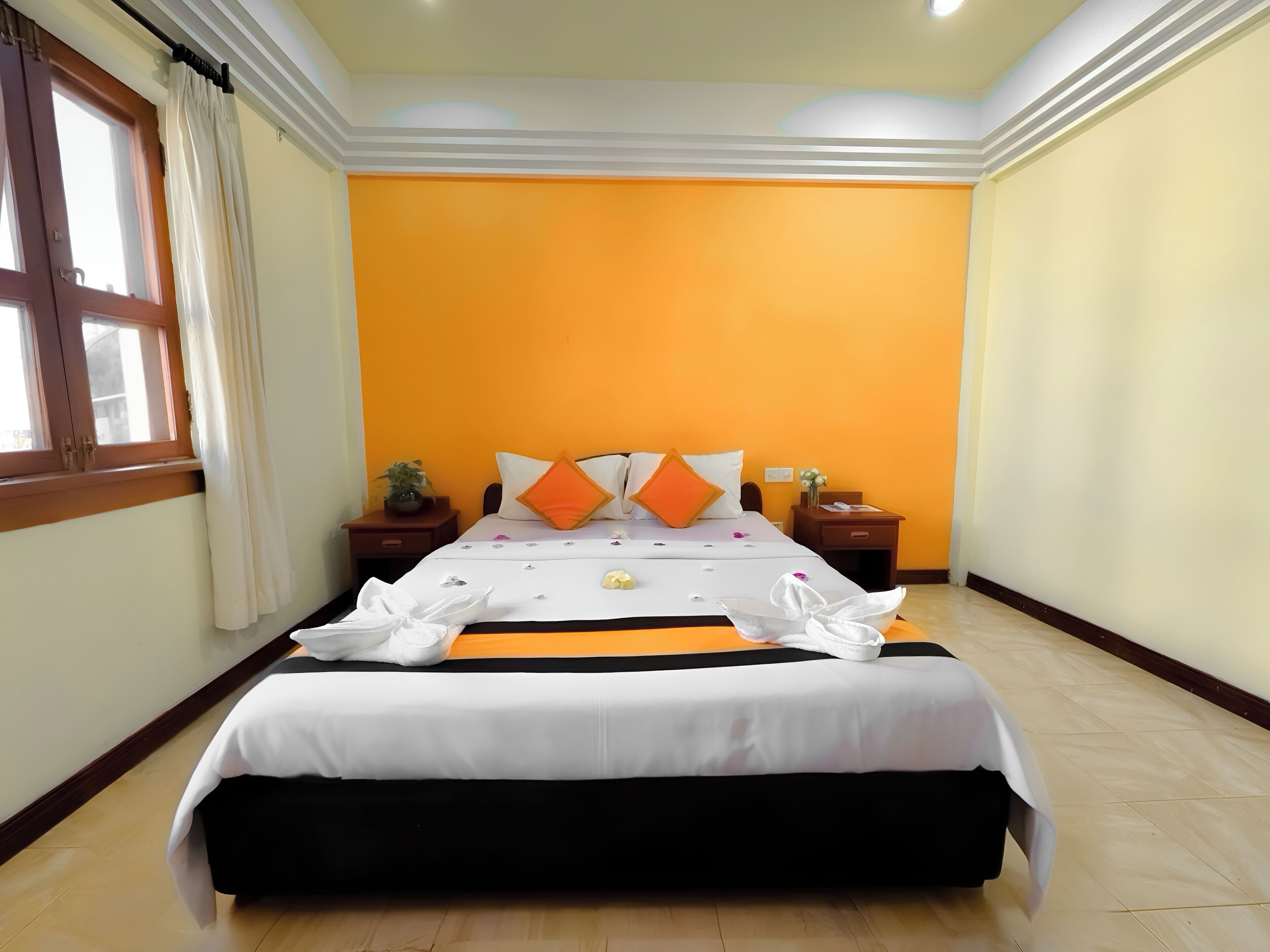 Una habitación de hotel con una cama grande, dos mesitas de noche, una ventana con cortinas y una pared de color naranja brillante.