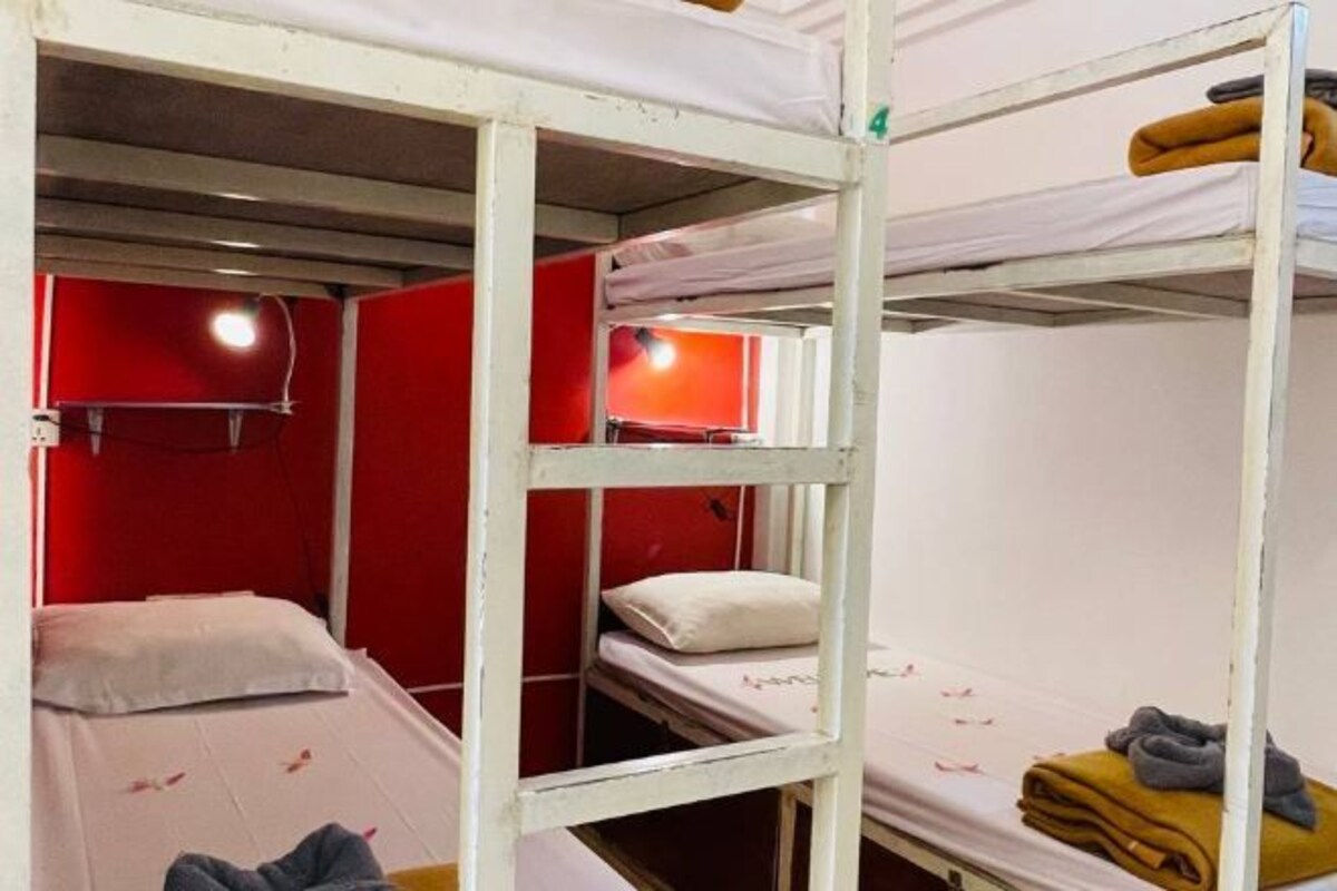 Une chambre avec un lit superposé, les murs peints en rouge, un plafond blanc et un lit simple sur la couche supérieure.