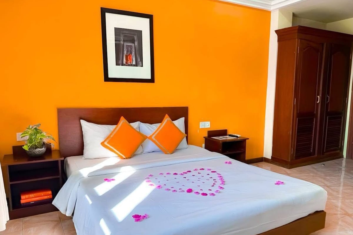 A hotel room with a bed, orange walls, a framed picture on the wall, and a wardrobe.