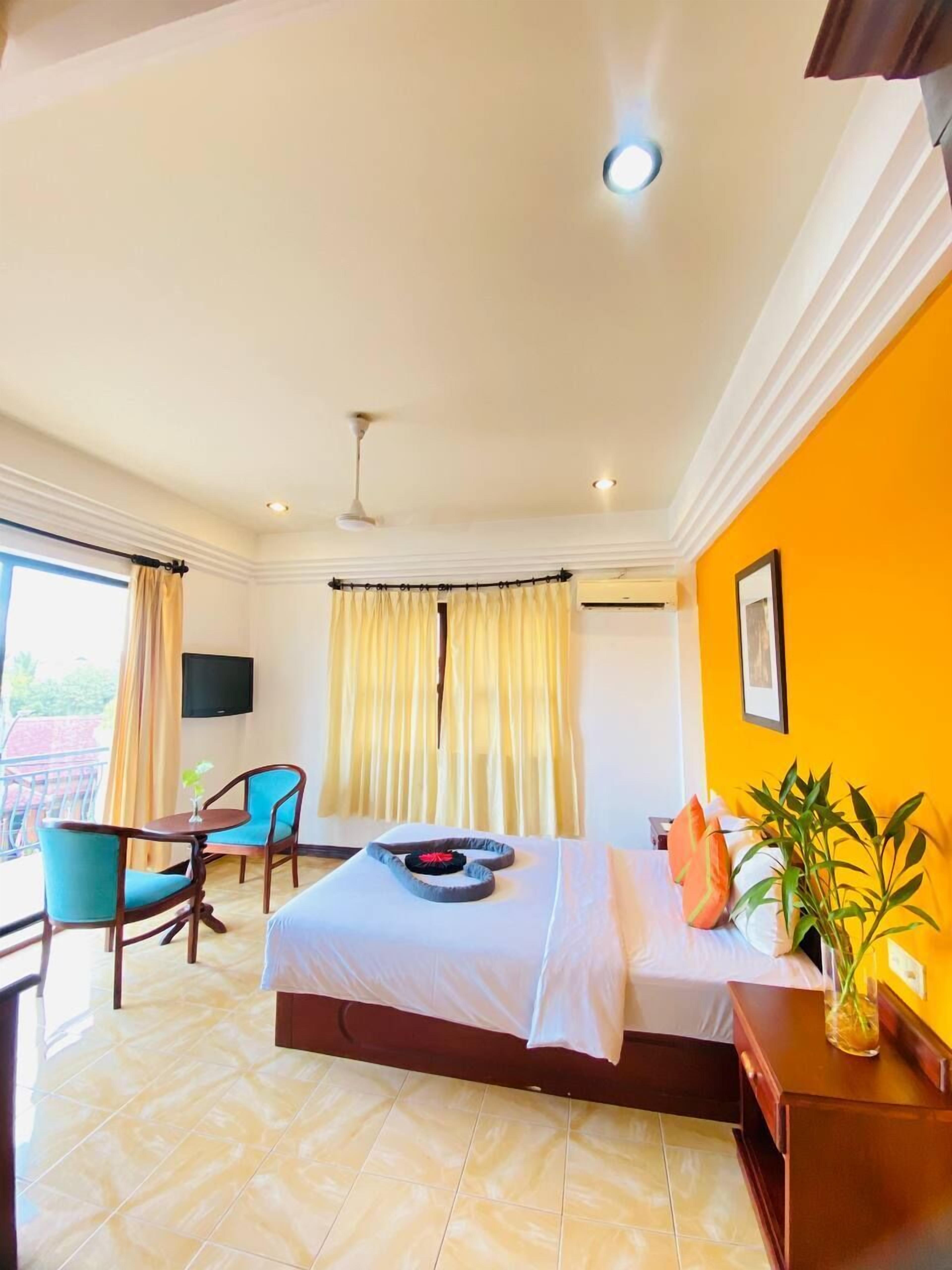 A hotel room with a bed, a desk with chairs, a TV, and a window with curtains.