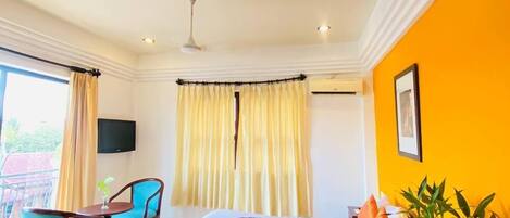 A hotel room with a bed, a desk with chairs, a TV, and a window with curtains.
