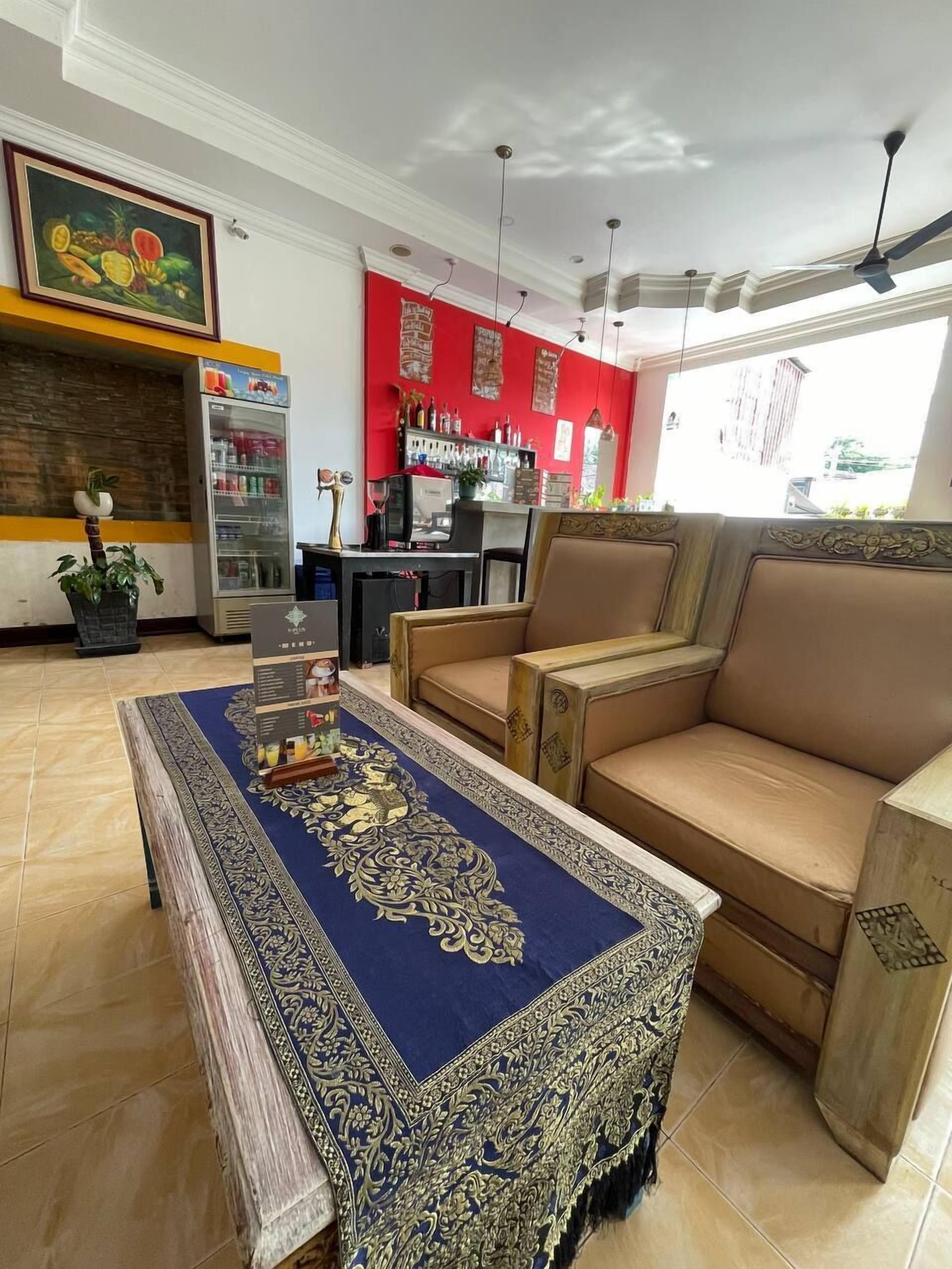 A living room with a sofa, a coffee table with a blue patterned runner, a refrigerator, a television, and a bar area with bottles.