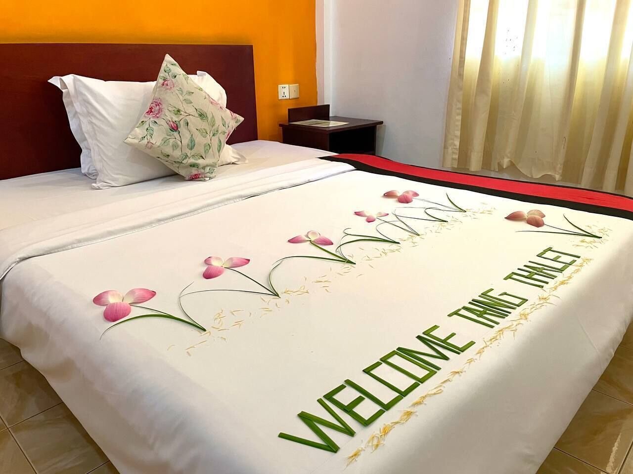 A neatly made bed with a floral arrangement and a welcome message.