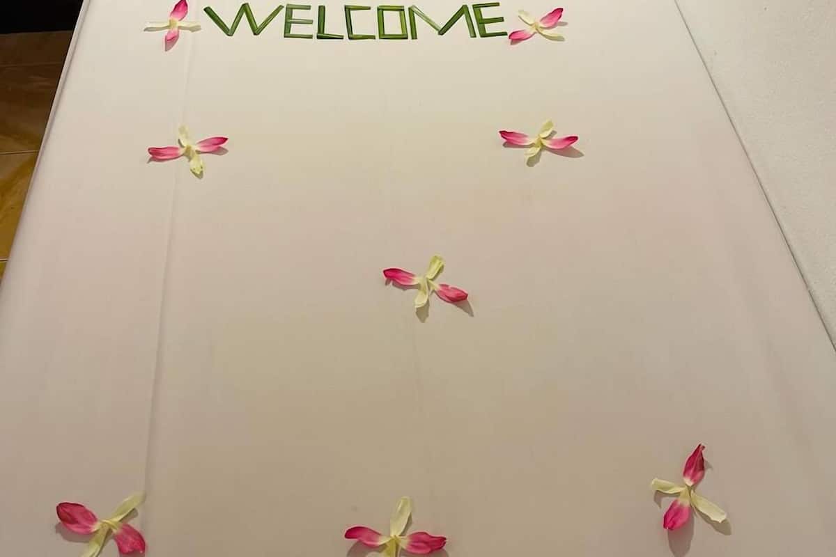 Ein Bett mit einem weißen Kopfkissen und einem 'WELCOME'-Schild aus Blumen.
