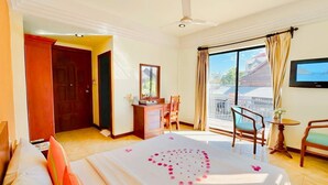 Een hotelkamer met een bed, een bureau, een stoel, een televisie en een balkon met uitzicht.