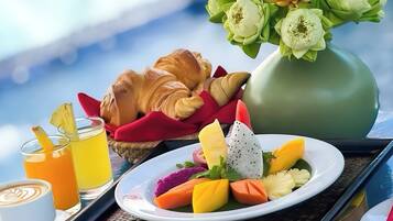 A breakfast tray with croissants, fruit, and juice, a vase of flowers, and a coffee cup.