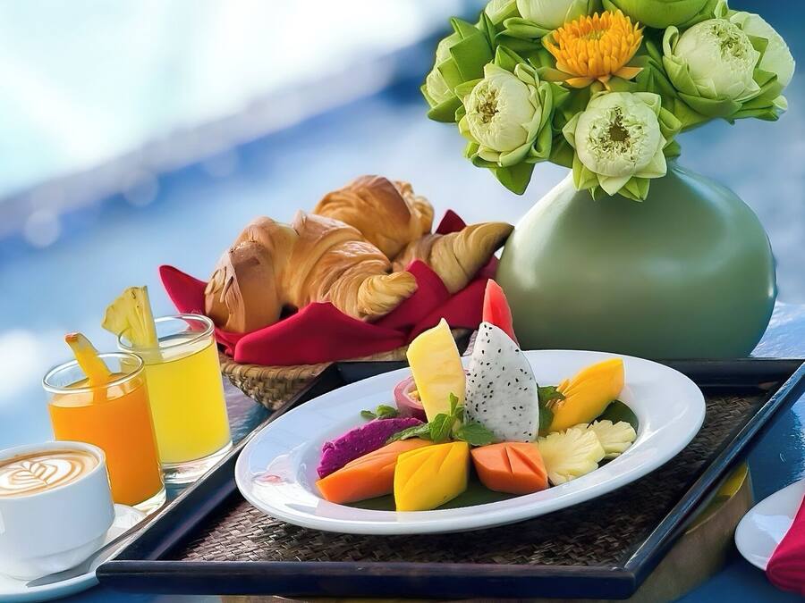 A breakfast tray with croissants, fruit, and juice, a vase of flowers, and a coffee cup.