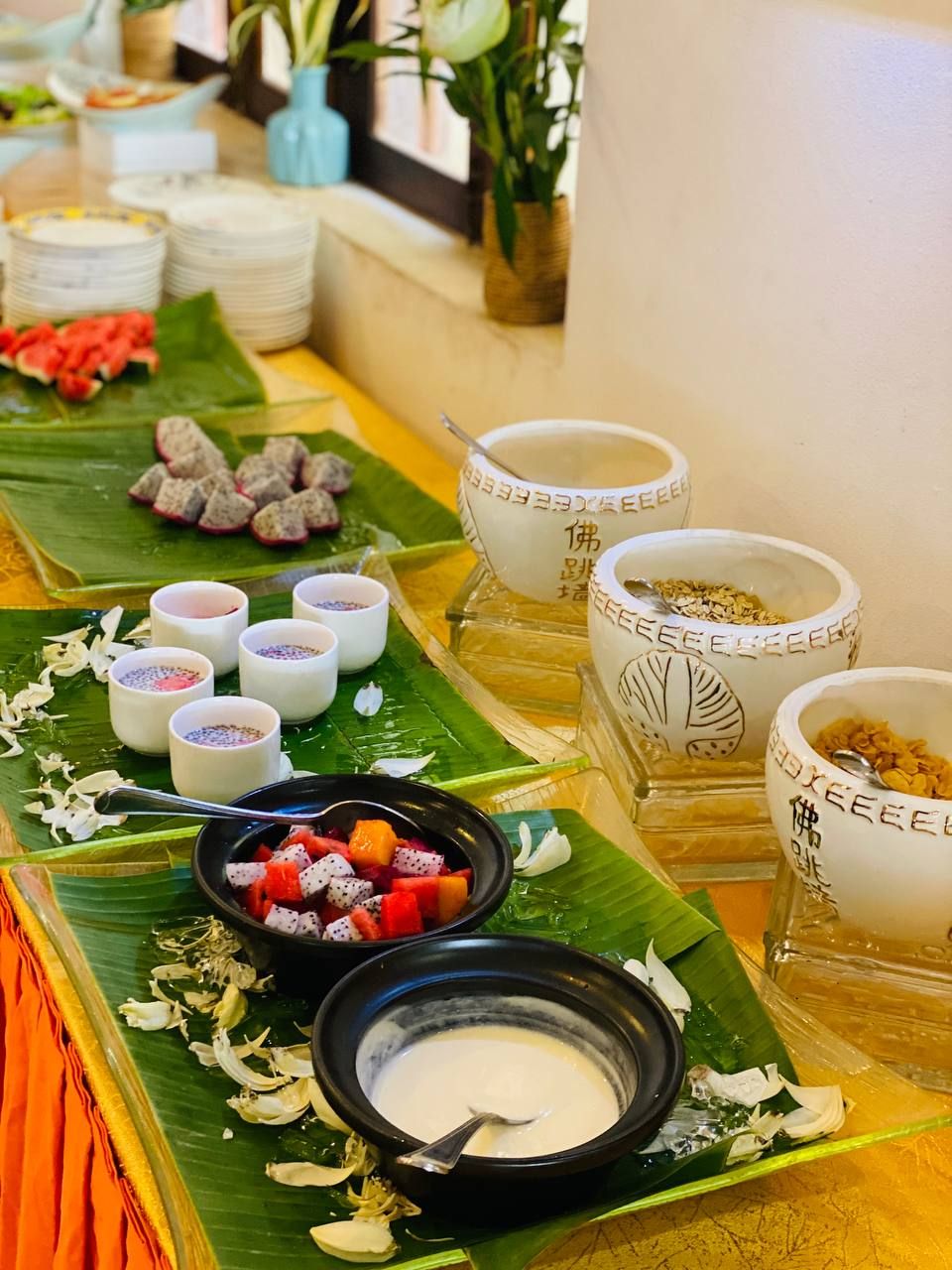 A buffet table with various dishes, including a bowl of mixed fruits, several small bowls with different food items, and a black bowl with a creamy substance.