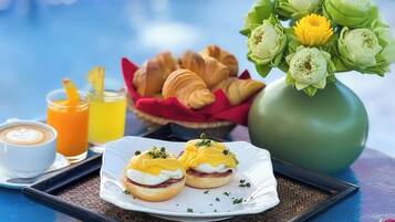 A breakfast tray with eggs Benedict, croissants, and a vase of flowers.
