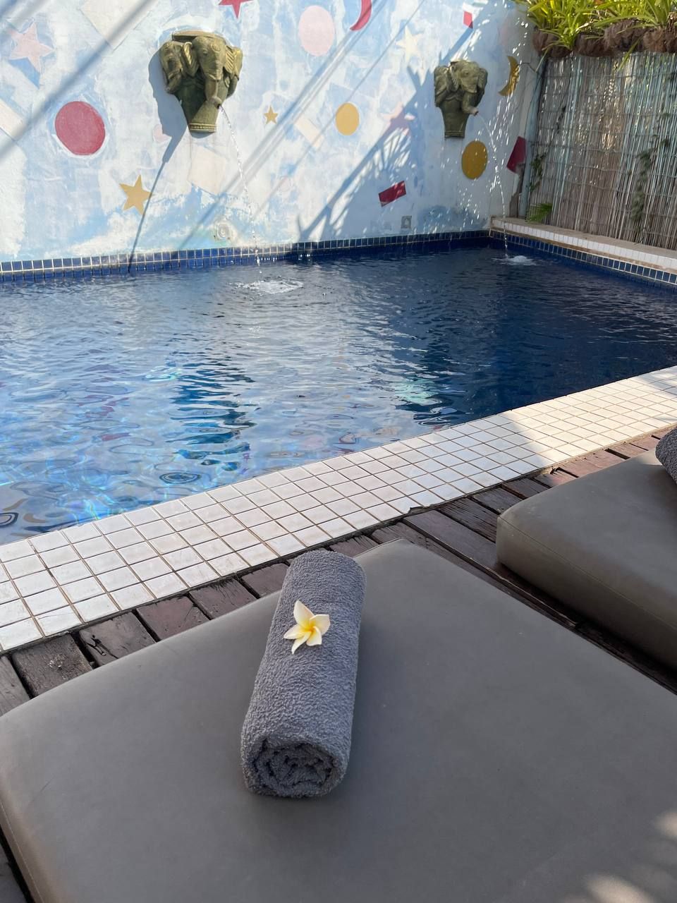 Un espace piscine avec une bordure carrelée, une serviette ornée de motifs floraux et des sculptures en pierre sur le mur.