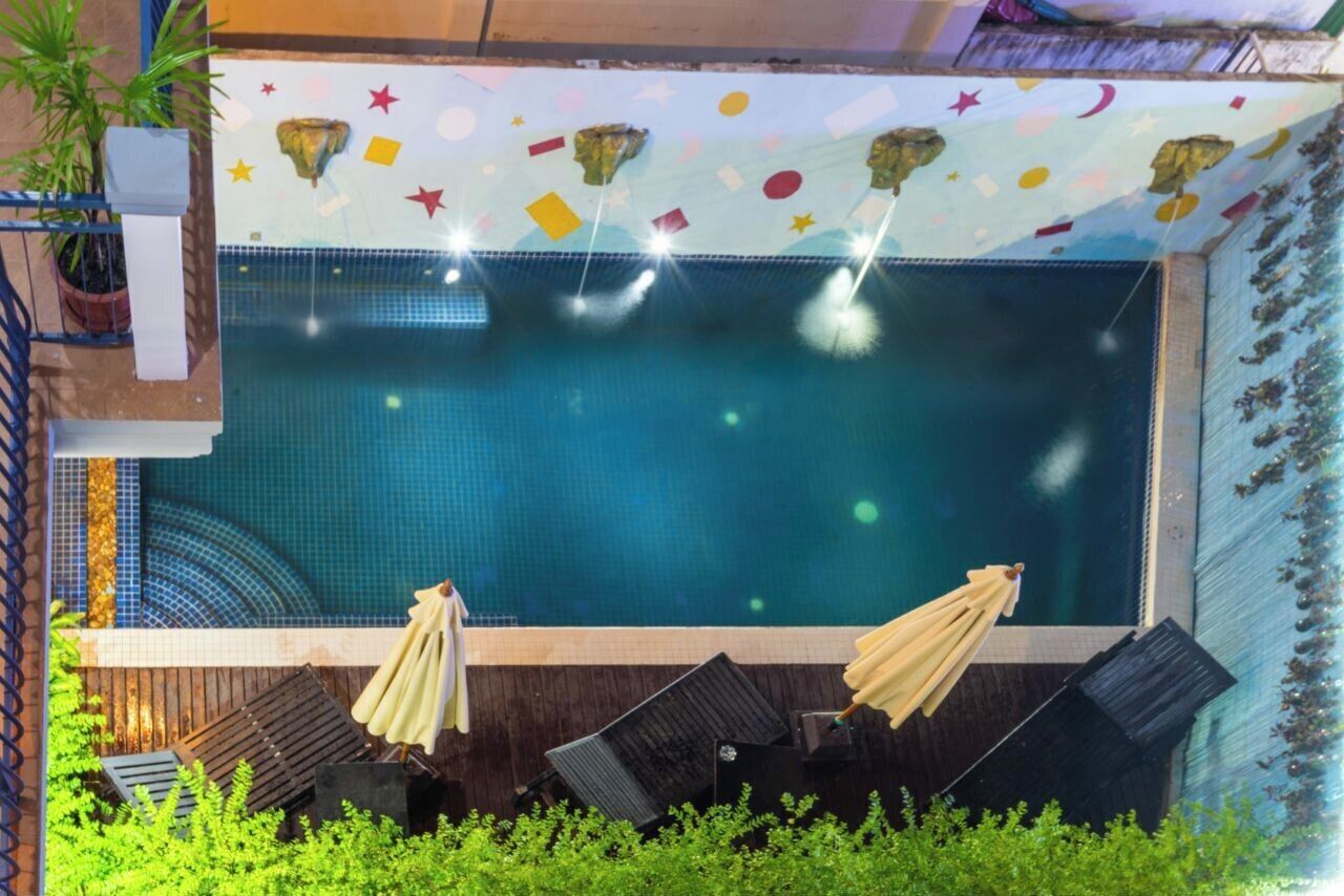 Una piscina con piso de baldosas, rodeada de sillas de descanso y sombrillas, y un techo decorado con estrellas y figuras.