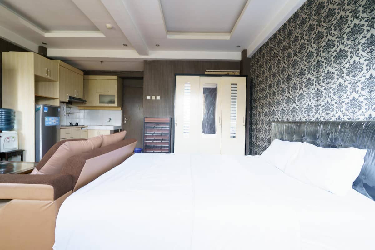 A modern hotel room with a large bed, a seating area with a sofa, a kitchenette, and a patterned wall.
