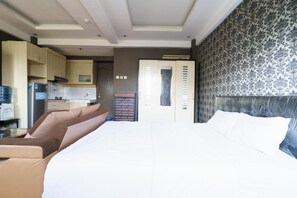 Una habitación de hotel moderna con una cama grande, una zona de estar con sofá, una kitchenette y una pared con diseño.