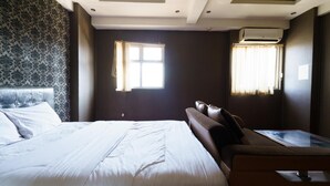 A hotel room with a large bed, a sofa, a small table, and two windows with curtains. - OYO 94238 The Suite Metro Apartment By Riz Living (Bandung)