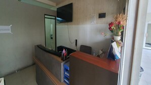A reception area with a wooden reception desk, a flat-screen TV mounted on the wall, and a flower arrangement on the desk. - OYO 94238 The Suite Metro Apartment By Riz Living (Bandung)