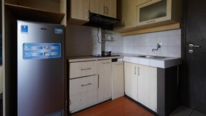 A compact kitchen with light wood cabinets, a stainless steel refrigerator, and a white countertop. - OYO 94238 The Suite Metro Apartment By Riz Living (Bandung)