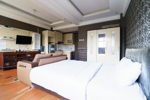 Un dormitorio con una cama grande, un sofá, televisión y una kitchenette.