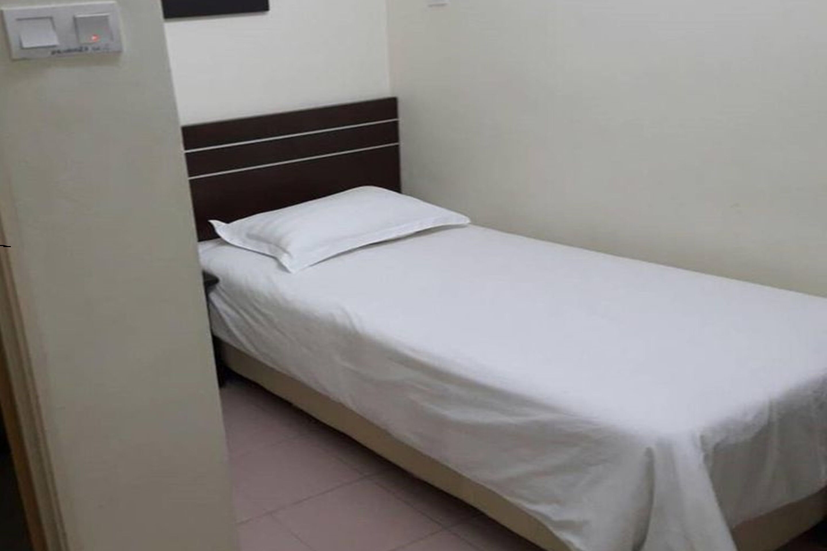 A small, single-bed room with a plain white wall and a brown headboard.