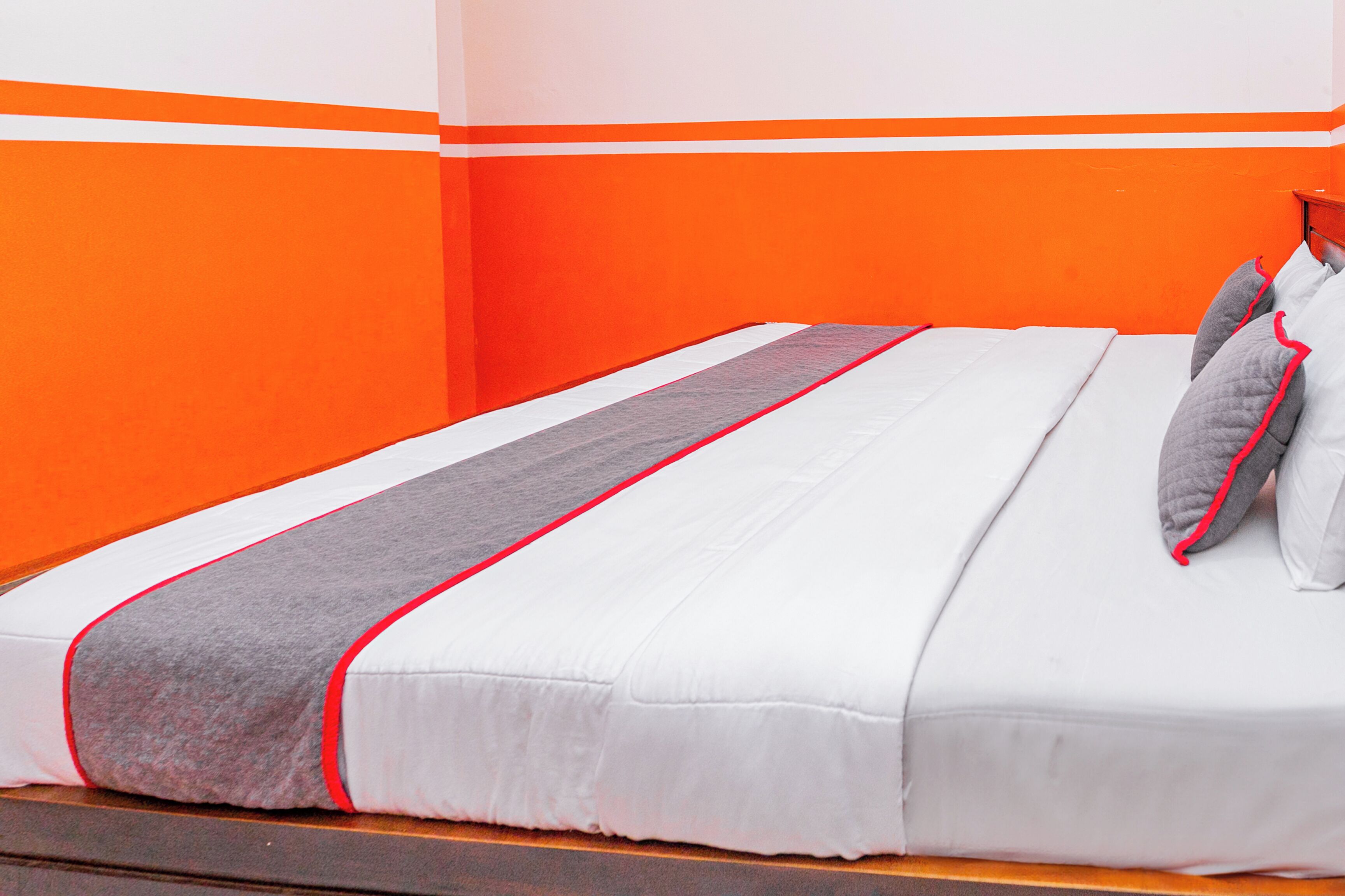 A bed with white bedding, grey and red accents, and grey pillows.