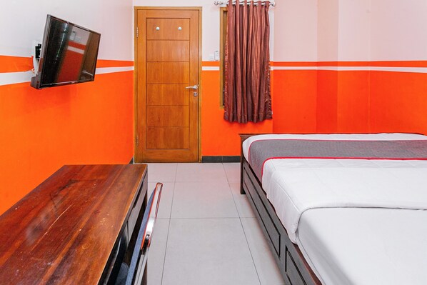 A hotel room with a wooden door, a flat-screen TV mounted on the wall, a bed with white bedding, and orange and white striped walls. - Hotel O Bang Day Residence (Depok)