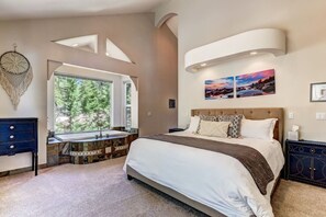 A bedroom with a large bed, a vanity with a sink, a window with a view of trees, and a wall-mounted light fixture.