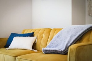 A yellow sofa with three pillows in a neutral room.