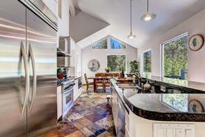 A modern kitchen with a large island, stainless steel appliances, and a dining area with a view of the outdoors.