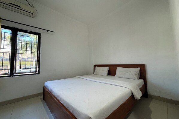 A single bed with white bedding in a room with white walls and a window with metal bars. - Hotel O Ezhar Boka Homestay Near GOR Sulis Bulutangkis (Pallangga)