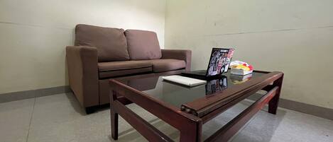 A living room with a brown sofa, a glass-top coffee table, and a magazine on the table.