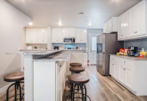 A modern kitchen with white cabinets, a central island with stools, a microwave, and a refrigerator. - Spacious 5-bedroom for Families Groups (Bethany)