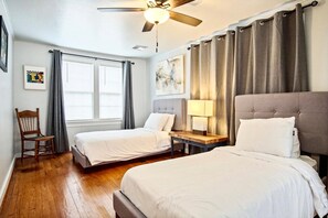 Two single beds with white linens, a ceiling fan, and a window with curtains.