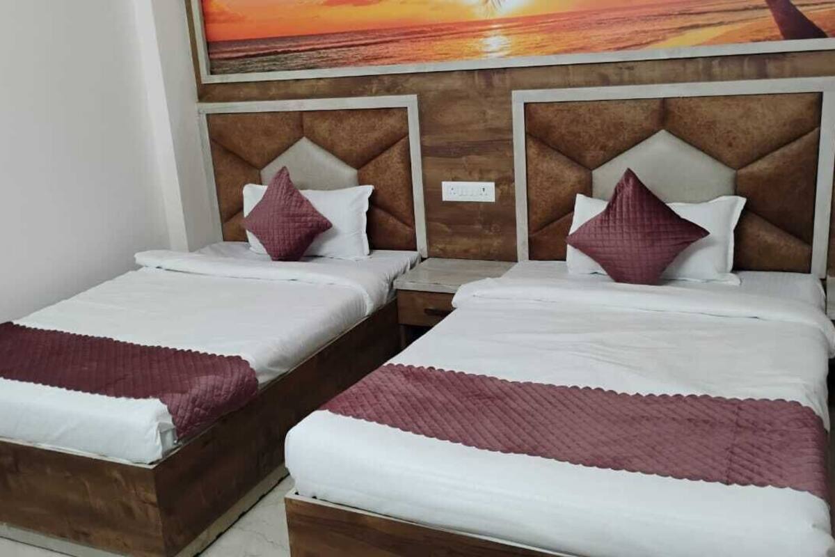 Deux lits simples avec des têtes de lit en bois et du linge de lit blanc, une table de chevet en bois et un grand tableau accroché au mur.