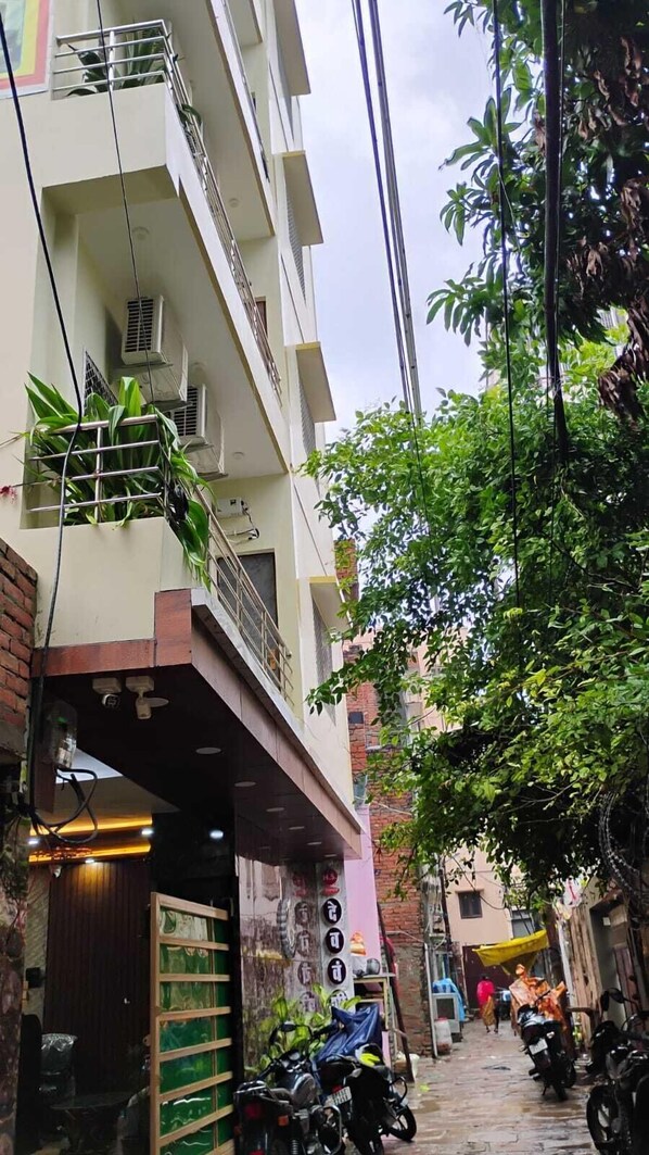 A narrow alleyway with a building on one side featuring a balcony with plants and a staircase. - Devvanshi Palace (Varanasi)
