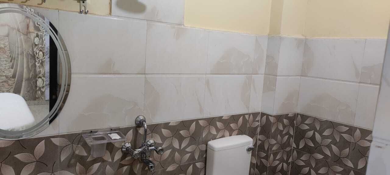 A bathroom with a toilet, sink, and mirror. The walls are tiled with a floral pattern.