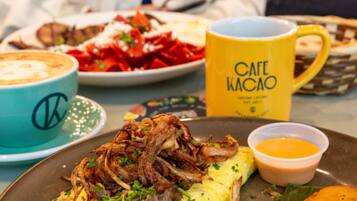 A meal with shredded meat, mashed potatoes, and a side of sauce, accompanied by a coffee cup and a yellow mug with text.