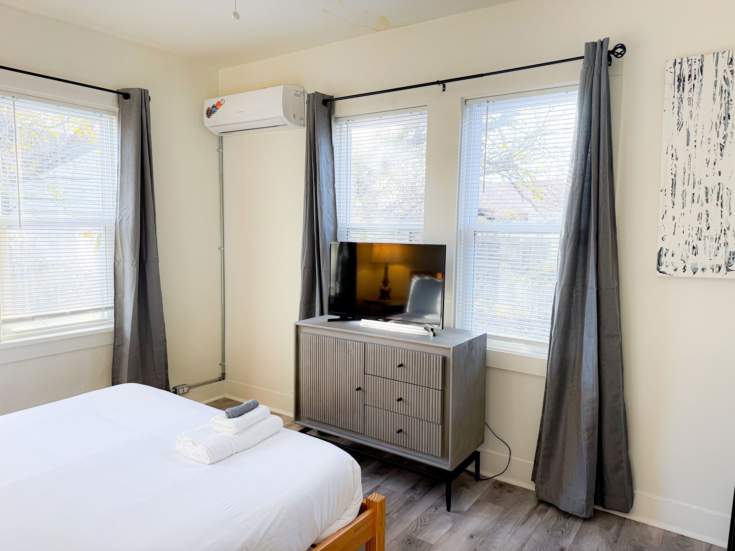 A hotel room with a bed, a dresser, a TV, and a window with curtains.