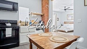 A modern kitchen with a brick wall, a microwave, a stove, and a dining table with two placemats. - Adorned Studio 3min-asian Dist Rain Shower (Oklahoma City)
