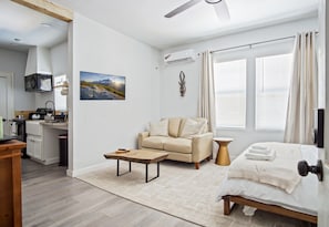 A modern hotel room with a bed, a sofa, a coffee table, and a view of the outdoors through large windows. - Adorned Studio 3min-asian Dist Rain Shower (Oklahoma City)
