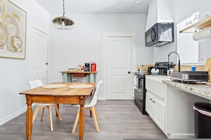 Et lille køkken med hvide skabe, et træspisebord og en hængende lampe.
