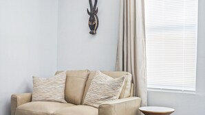 A beige sofa with patterned cushions, a small round table, and a wall-mounted decorative piece. - Adorned Studio 3min-asian Dist Rain Shower (Oklahoma City)