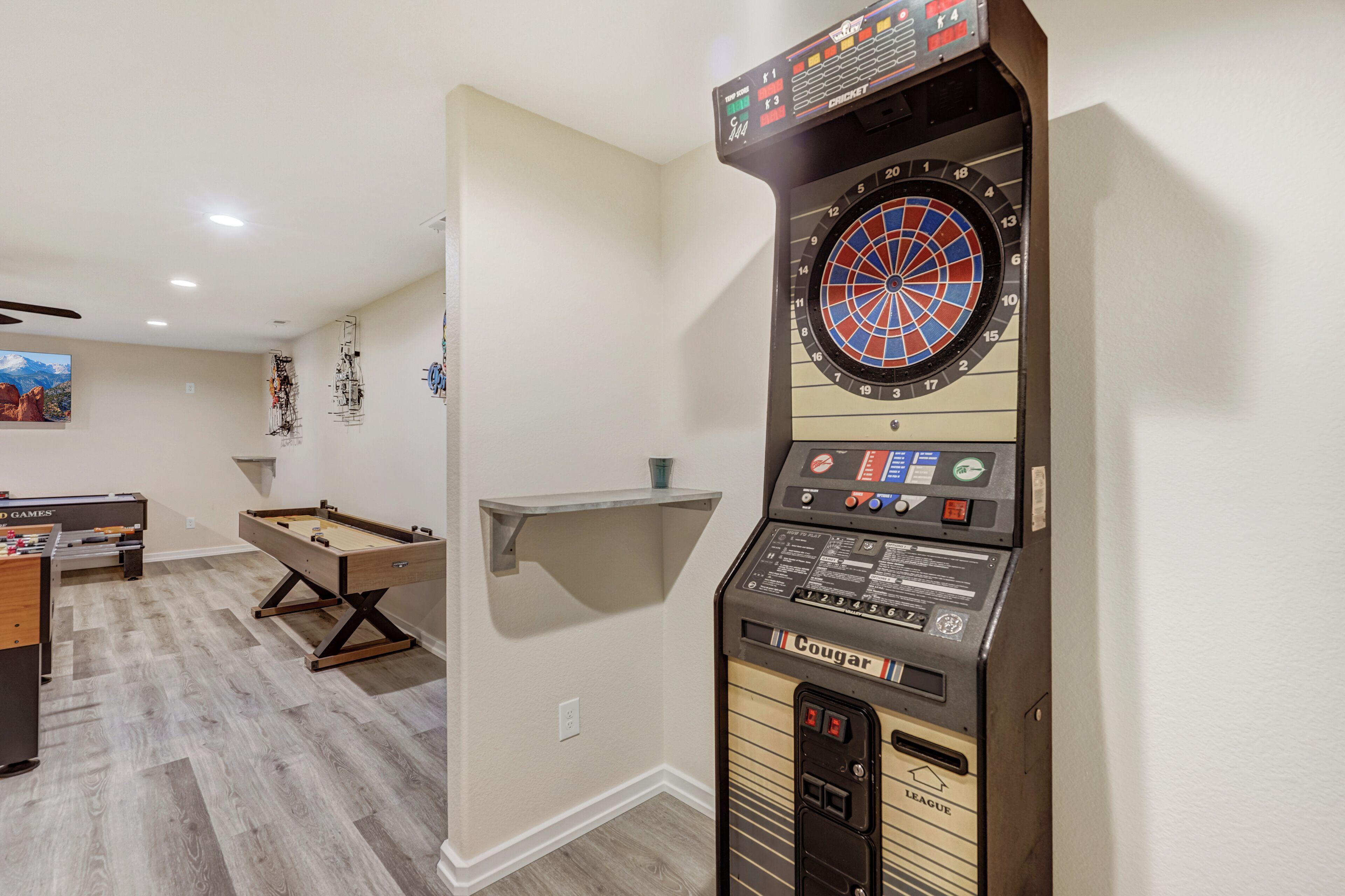 A room with a dartboard, foosball table, and pool table.