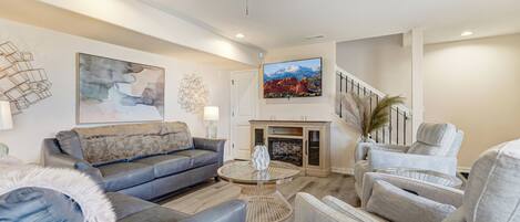 A modern living room with a grey sofa, a round glass coffee table, and a fireplace.