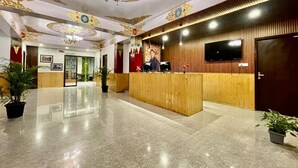 A hotel lobby with a reception desk, a large chandelier, and a TV mounted on the wall. - Voyage Royal Retreat (Gangtok)